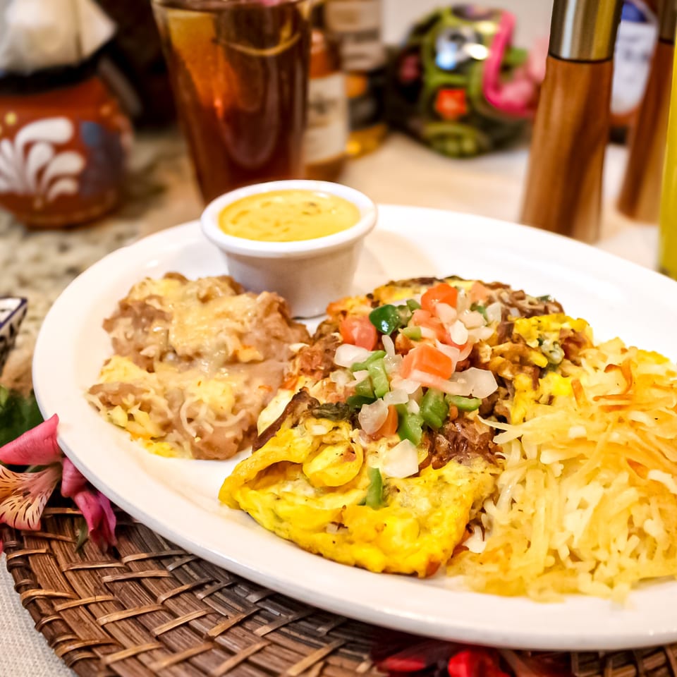Colorful Mexican-style platter with enchiladas, rice, beans, vegetables, and yellow sauce served on a white plate.