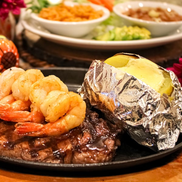 Mi Pueblito Cafe's steak and shrimp entree with a foil-wrapped baked potato and sides.