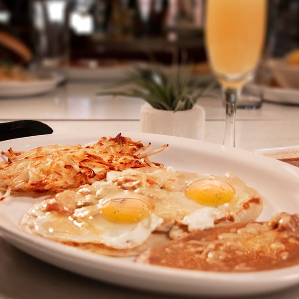 Breakfast plate with fried eggs, hash browns, and a mimosa at Mi Pueblito Cafe.