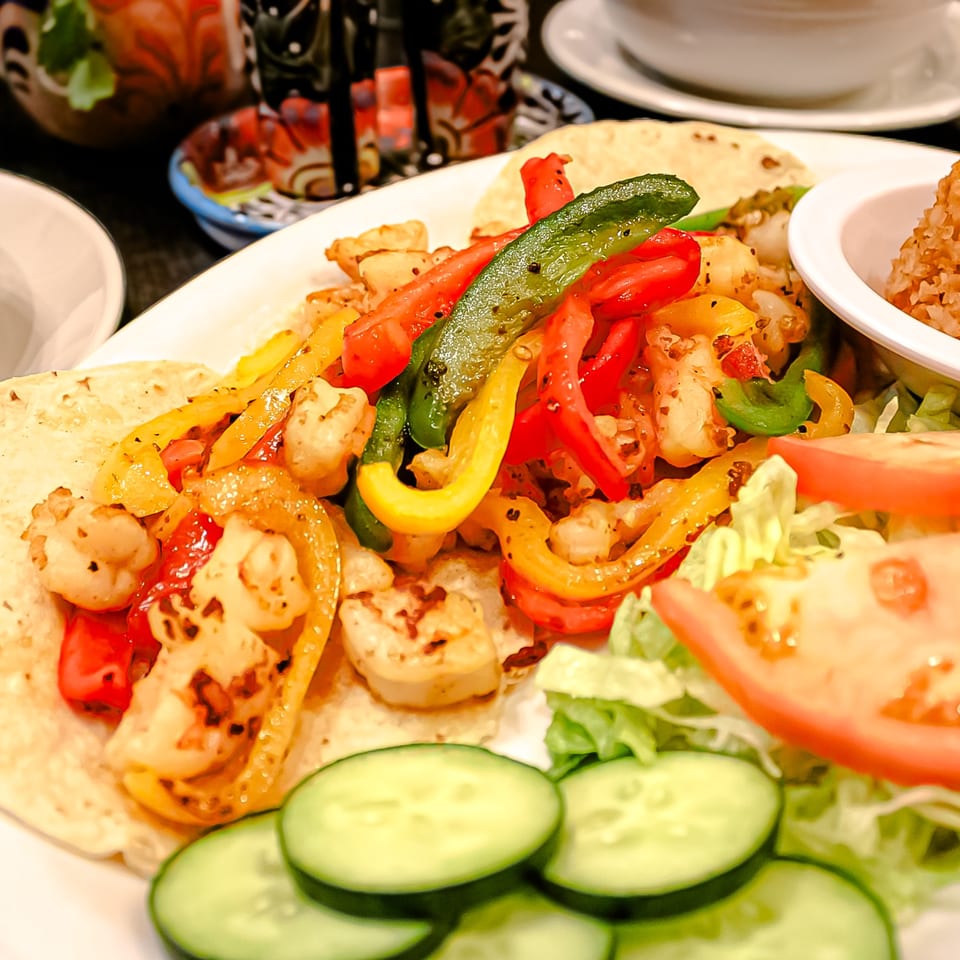 Grilled chicken fajitas with colorful peppers on tortillas, served alongside cucumber slices, salad, and rice.