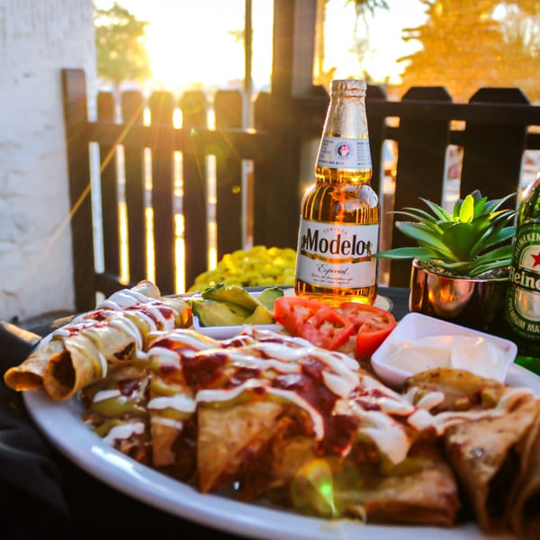 Mi Pueblito Cafe's enchiladas and taquitos with avocado, tomatoes, and Modelo beer at sunset.